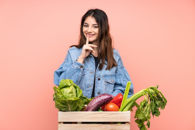 Young farmer woman holding a basket full of fresh vegetables doing silence gesture