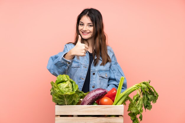 親指ジェスチャーを与える新鮮な野菜がいっぱい入ったかごを保持している若い農家の女性