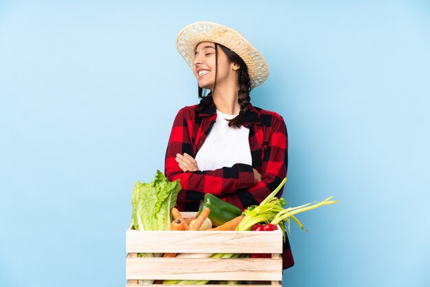 幸せと笑顔の木製バスケットに新鮮な野菜を保持している若い農家の女性