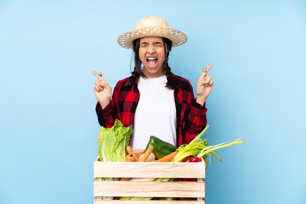 Young farmer Woman holding fresh vegetables in a wooden basket with fingers crossing