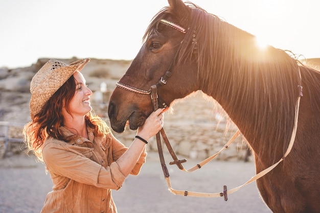 Young farmer woman playing with her bitless horse in a sunny day inside corral ranch