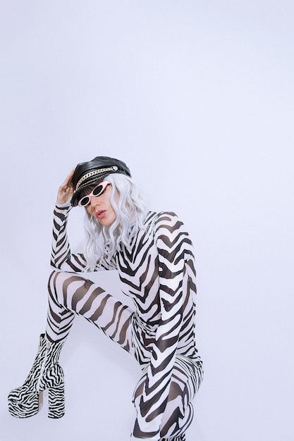 Young Fashion androgene blonde model in freak stijlvolle zebra print kleding en laarzen poseren in een witte studio. Accessoire trend leren pet