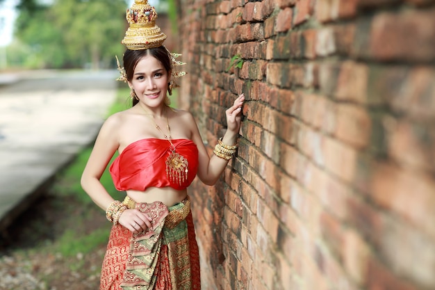 Young fashion asian girl in thai traditional costume standing\
with ancient brick wall