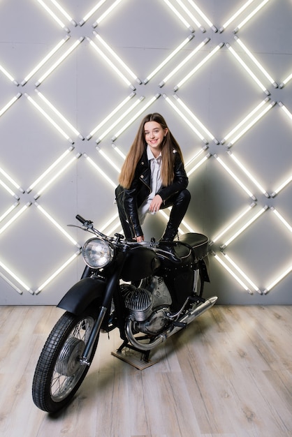 Young fashion girl posing in a black leather with motorcycle.