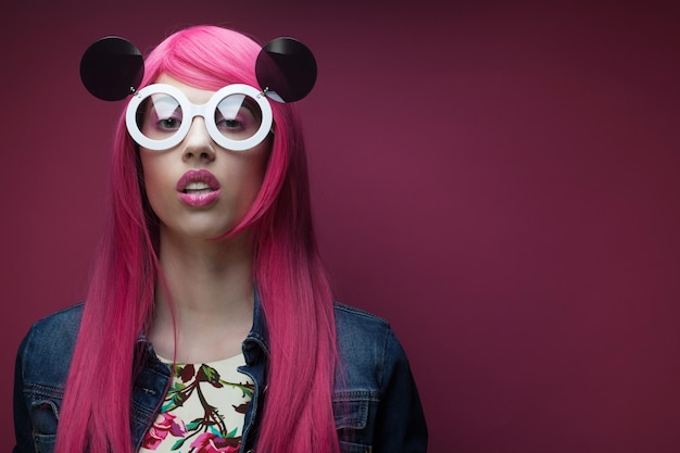 Young fashion girl with pink hair and big sunglasses over pink background