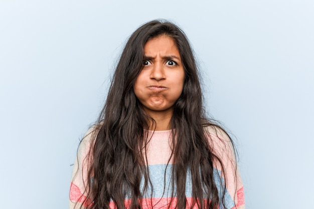 Young fashion indian woman blows cheeks, has tired expression. Facial expression concept.