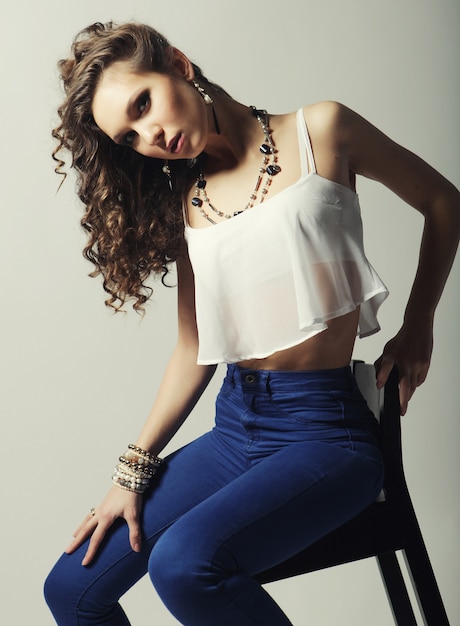 Young fashion model sitting on chair, studio shot