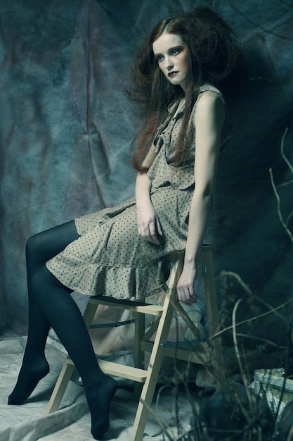 Young fashion model sitting on a stool in drama decoration