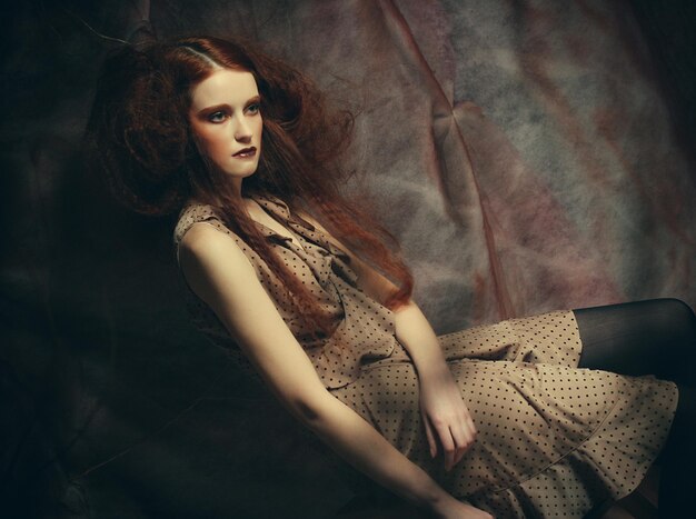 Young fashion model with creative make up sitting on a stool in