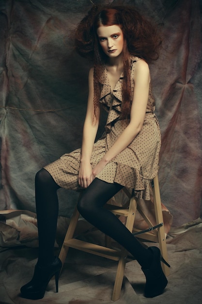 Young fashion model with creative make up sitting on a stool in
