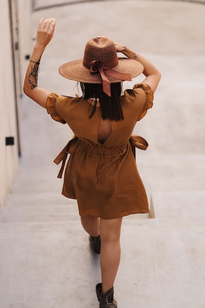 Фото Молодая модница, одетая в летнее платье с широкой плетеной шляпой, ходит и позирует в старом городе.