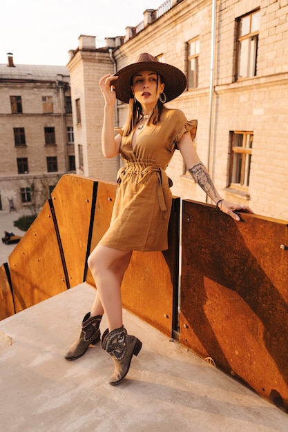 Young fashion woman dressed in a summer dress with a wicker wide hat walks and poses in the old city.