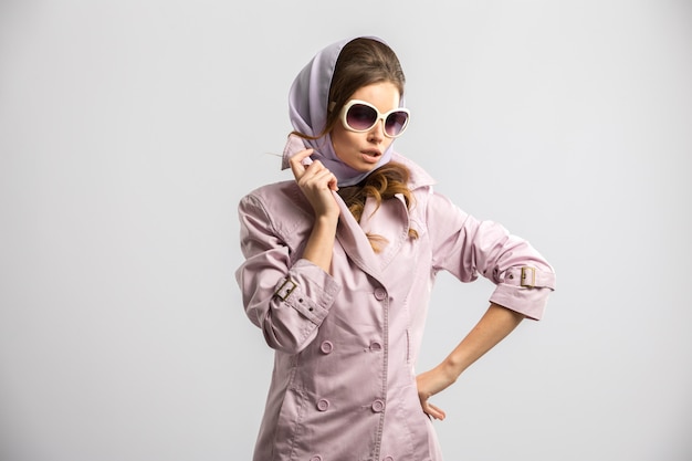Young fashion woman posing wearing pink coat and white sunglasses