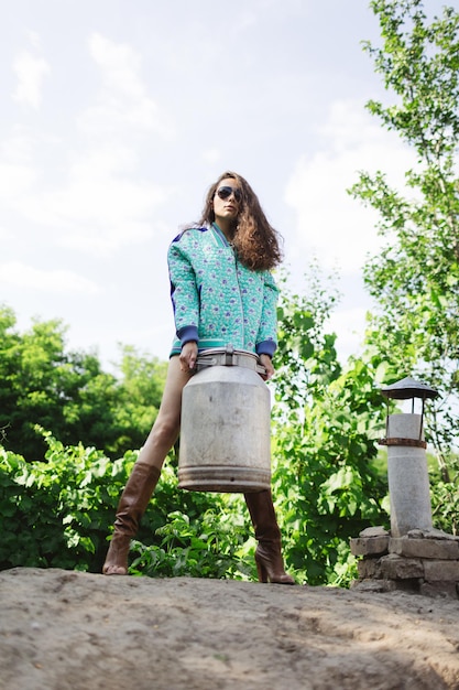 Young fashionable farmer woman posing on camera while holding milk can