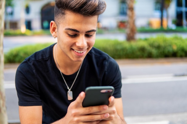 Young fashionable handsome man on the street of modern city chatting and typing on a cell phone. Communication and messenger concept