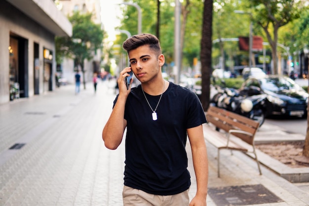 Young fashionable handsome man on the street of modern city talking on a cell phone. Communication concept