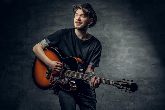 Young fashionable hipster blues and jazz acoustic guitar player with tattoos on his arms playing melody.