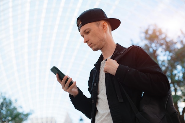 Young fashionable modern guy a man in a black cap and sunglasses with a smartphone talks on the phone on a city urban background in a tunnel in the sunset rays of the sun