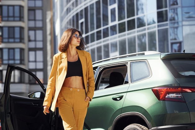 Young fashionable woman in burgundy colored coat at daytime with her car