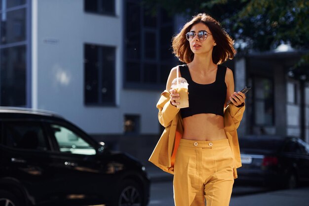 Young fashionable woman in burgundy colored coat at daytime\
with her car