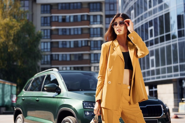 Young fashionable woman in burgundy colored coat at daytime with her car