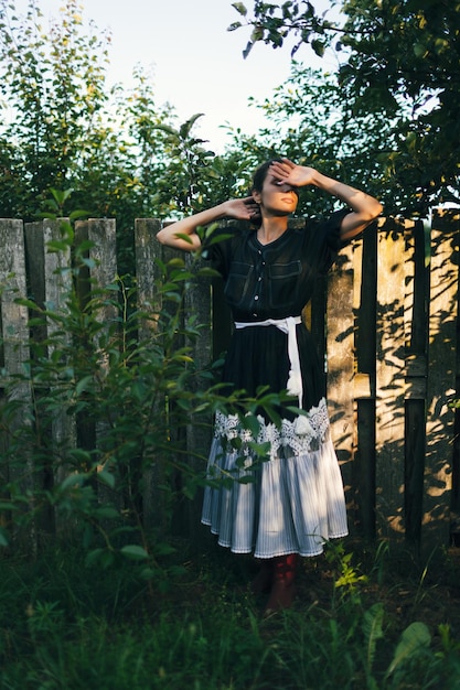 Young fashionable woman stands near fence in the garden or backyard of countryside house Summer time routine relax harvest concept