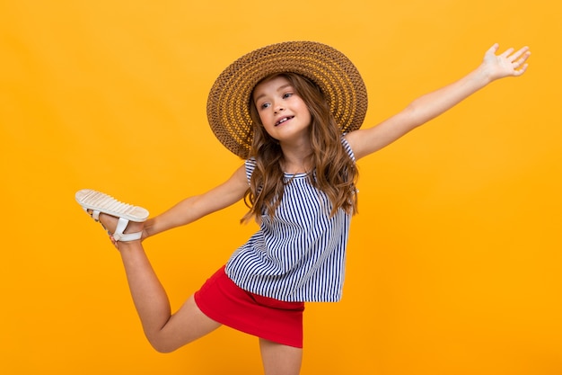 Young fashionista girl flirts in a straw hat on a yellow background with copy space.