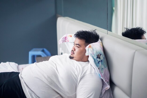 Young fat man looks pensive on the bed