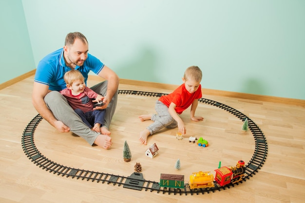 写真 若い父と子供たちが一緒に楽しんでいます。家族はプレイルームでおもちゃの鉄道を遊ぶ