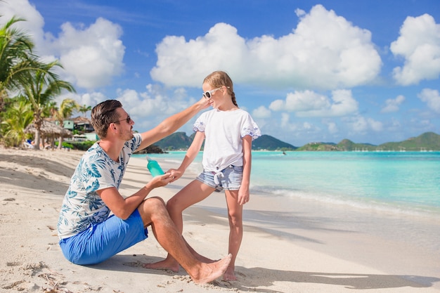 Young father applying sun cream to daughter nose on the beach. Sun protection