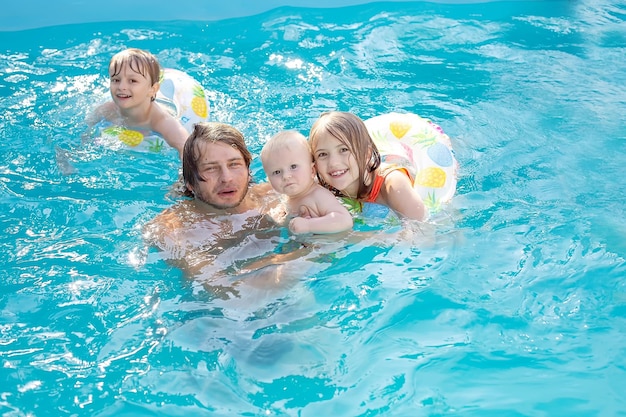 a young father in an embrace with his children daughter and son swims in the pool