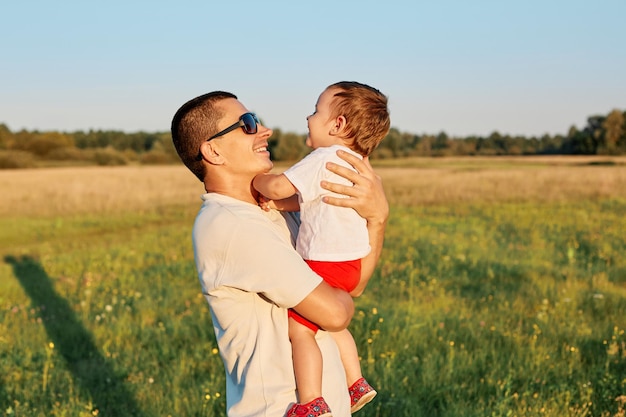 Young father and his infant daughter enjoying happy time and hot sunny days together in summer green meadow daddy embracing charming baby girl