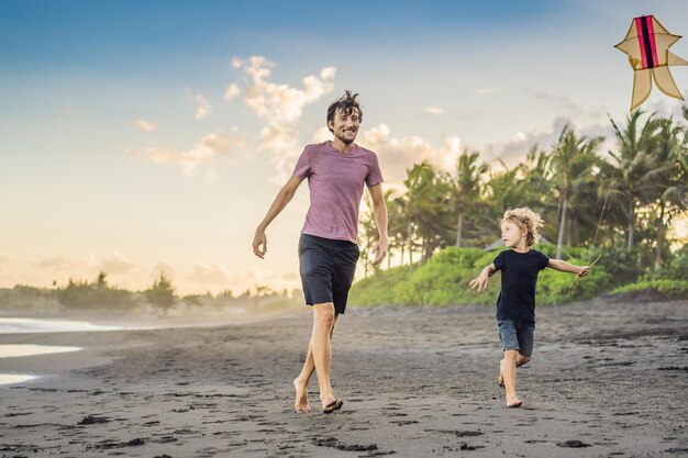 ビーチで凧と一緒に走っている若い父と彼の息子