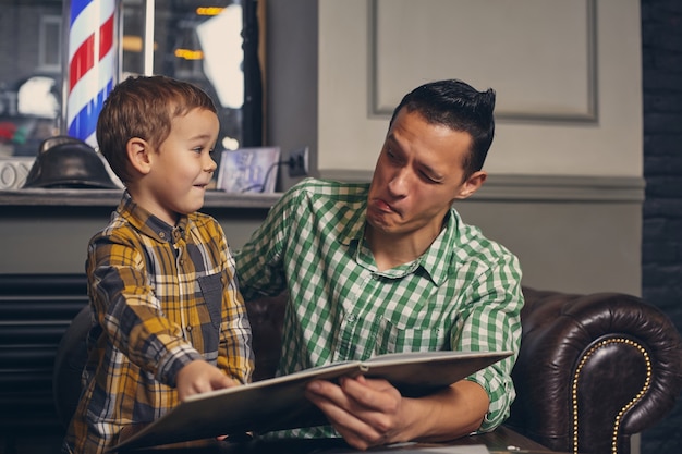 Young father and his stylish little son in the barbershop in the waiting room