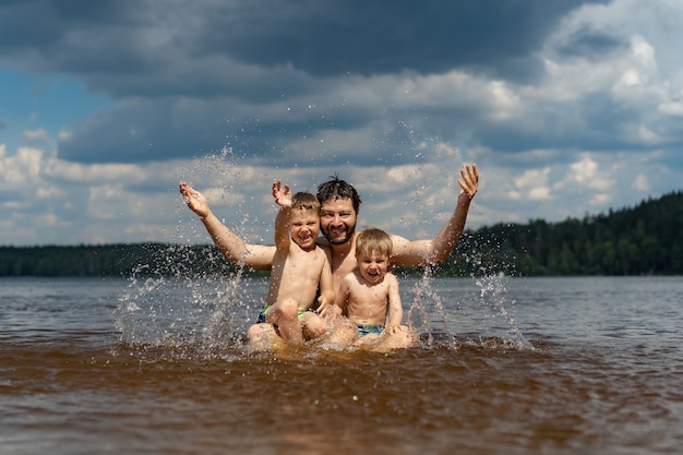 young father and his two little cute son sitting in the lake in forest and splashing