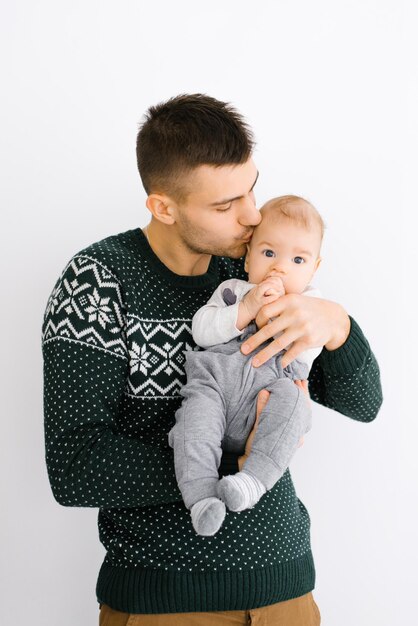 Photo a young father holds his little son in his arms and kisses him on a white background