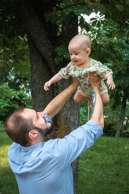 Young father is holding his baby son and playing with him close-up on the background of a summer landscape. Baby smiles and looks at daddy