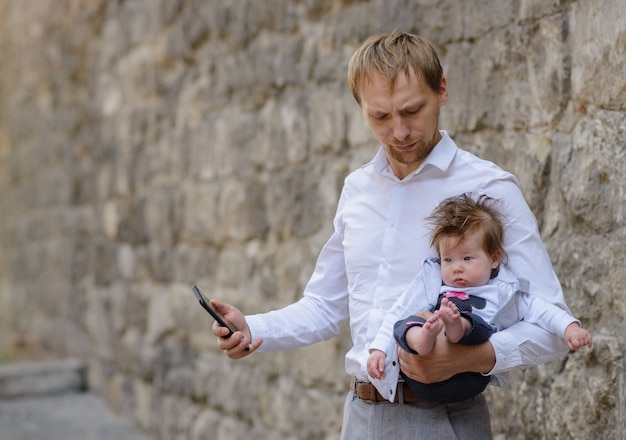 A young father is talking on a cell phone and holds his little daughter in his arms. copy space