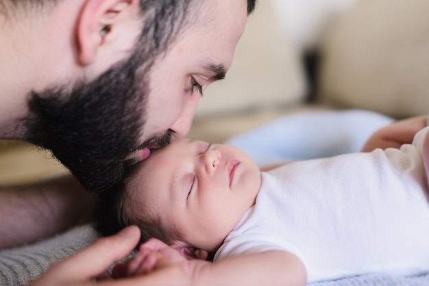 若い父親が彼の生まれたばかりの赤ちゃんにキスします。