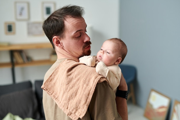 Young father looking at adorable baby son on his shoulder covered with napkin