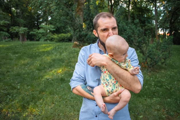 Foto giovane padre che gioca con suo figlio bambino sullo sfondo di un paesaggio estivo. papà morde il figlio scherzosamente e fa una smorfia