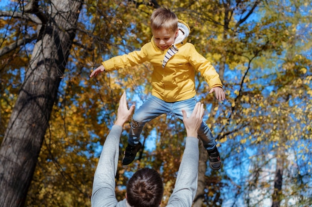 若い父親は、秋の公園で彼のかわいくて幼い息子を空中に投げます。高品質の写真