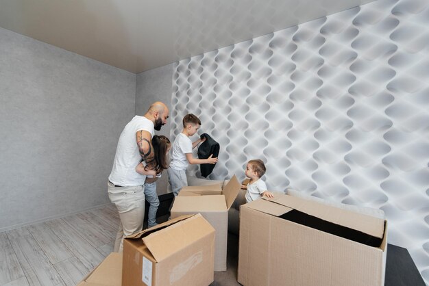 A young father with children unpacks a box of things after moving to a new apartment Purchase of real estate Housewarming delivery and transportation of goods