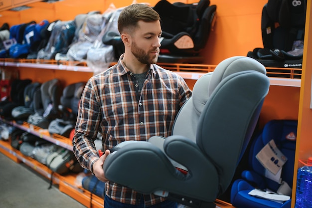 Young father with choosing car seat in store of childrens goods