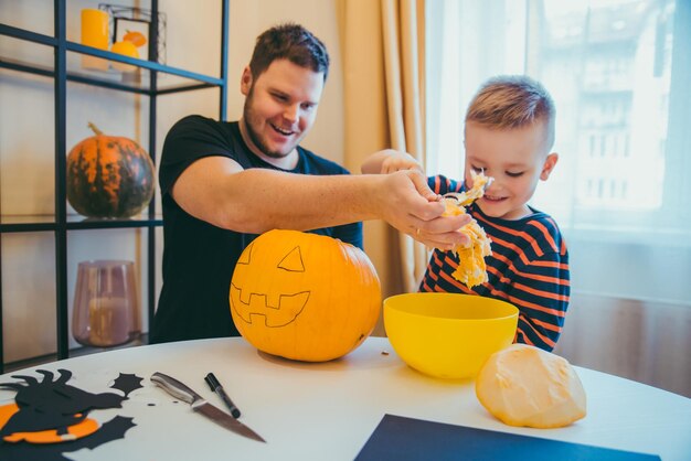 Молодой отец с маленьким сыном делают тыквенную голову на праздник хэллоуина