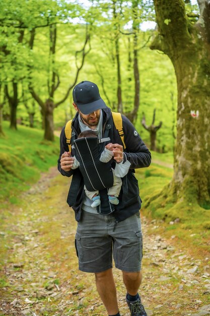 A young father with a yellow backpack walking with the newborn child in the backpack on a path in the woods