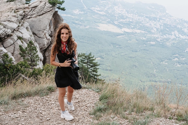 A young fearless woman photographer is a tourist high in the mountains near the abyss Active recreation Climbing the mountain