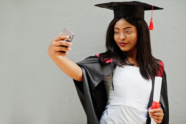 Young female african american student with diploma and mobile phone poses outdoors.