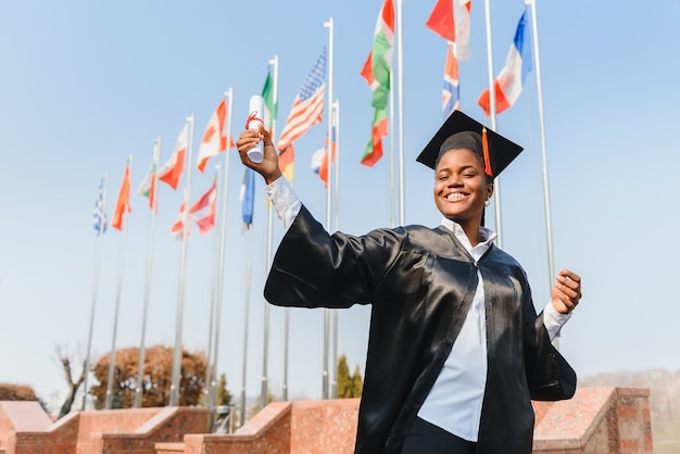 Молодая афро-американская студентка с дипломом позирует на открытом воздухе.
