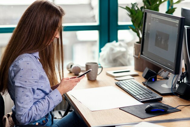 近代的なオフィスの職場でスマートフォンを使用して若い女性建築家。